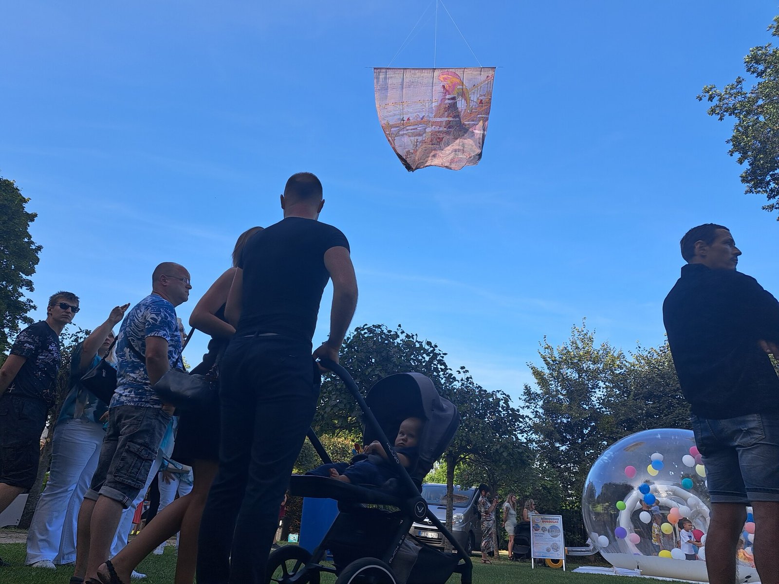 Pakuonio šventės lankytojai po danguje skrendančiu aitvaru su Čiurlionio paveikslu „Angelas“